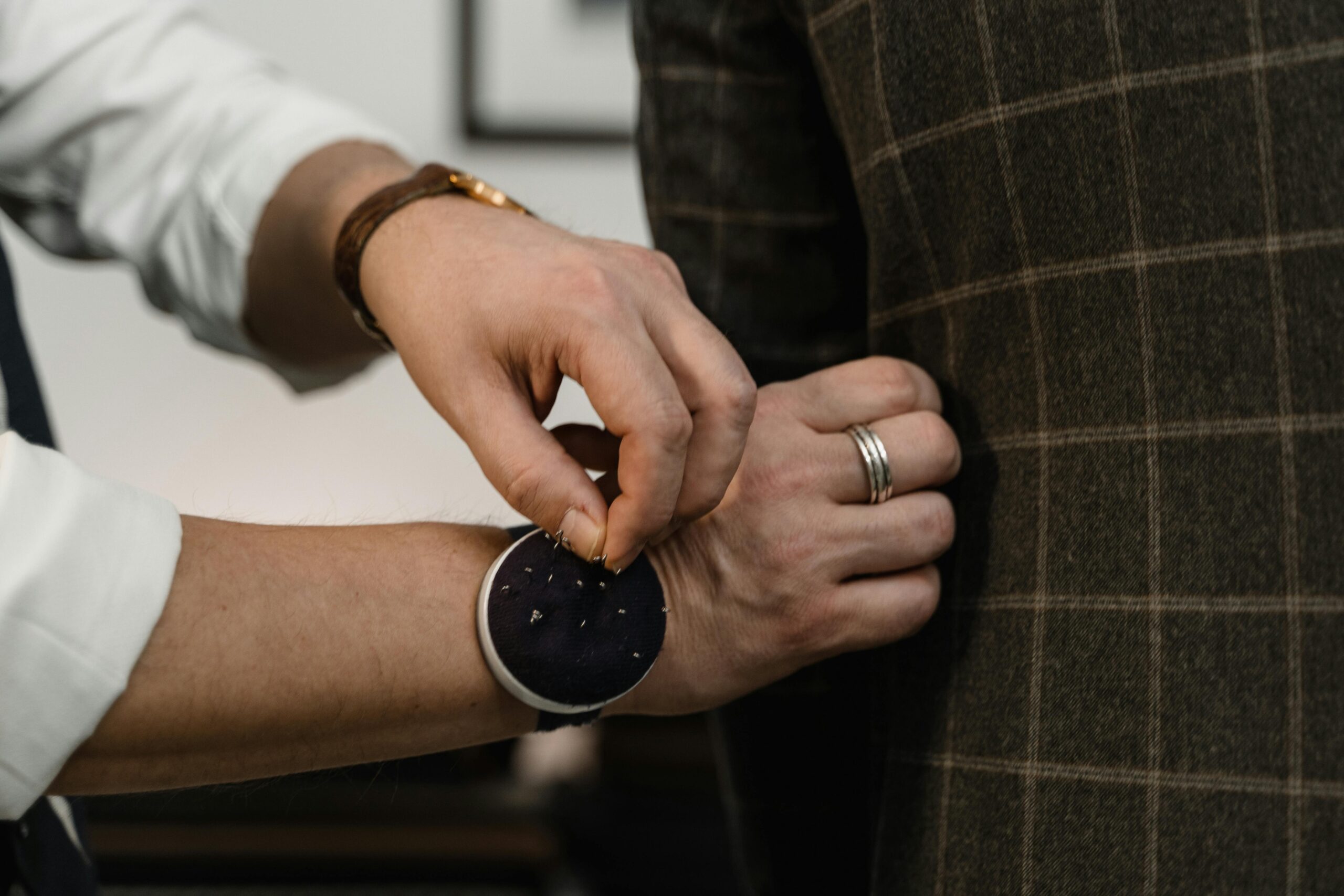 Close-up of a tailor adjusting a checkered suit jacket during a fitting session.